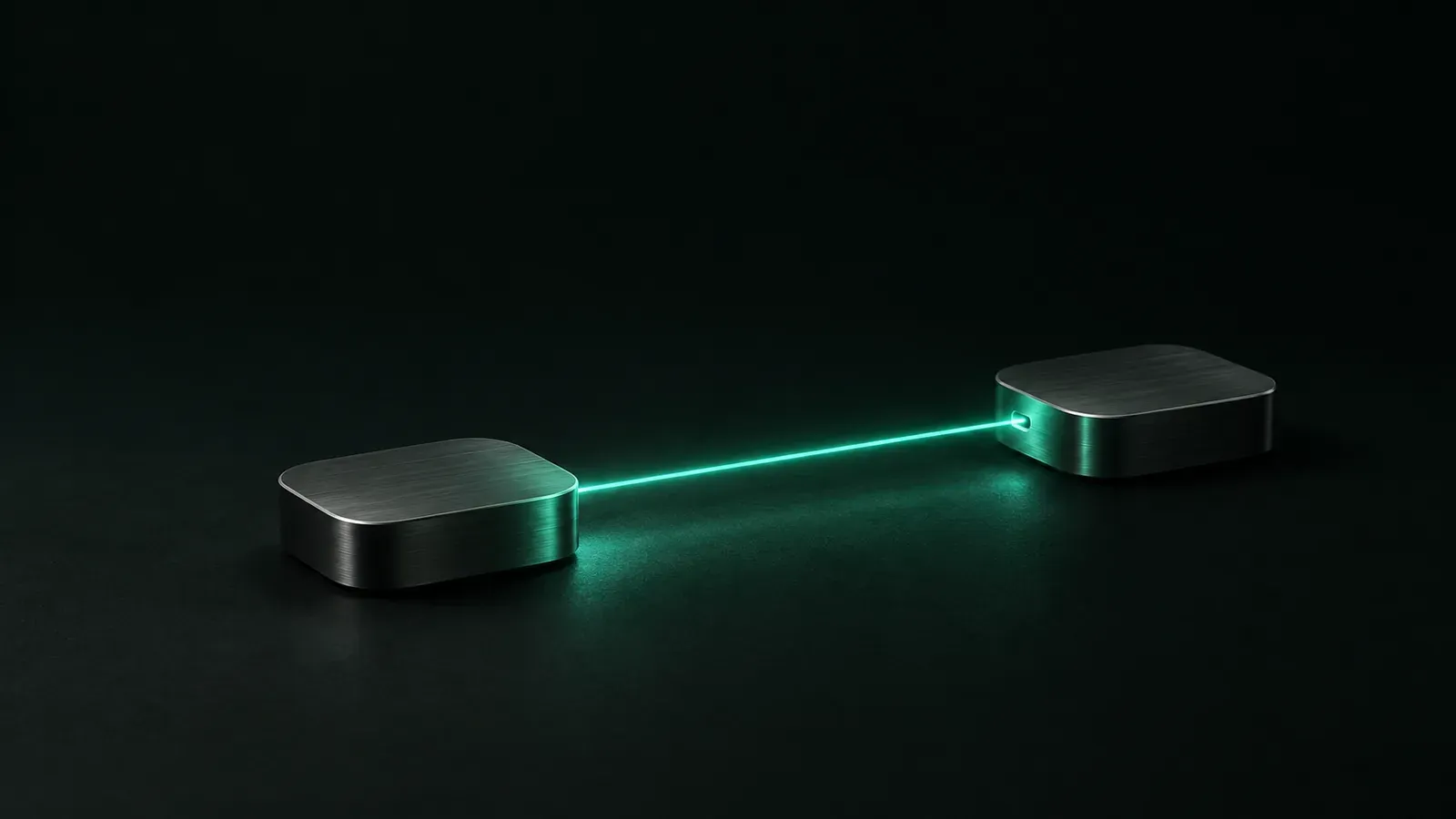Two small rounded aluminium boxes rest on a dark surface, connected by a thin straight beam of teal light.