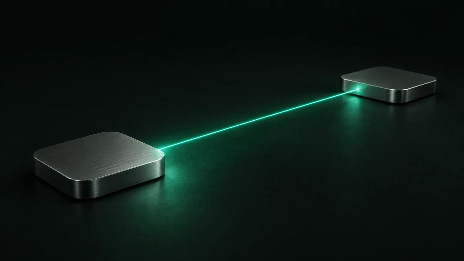 Two rounded aluminium boxes rest on a dark green surface, connected by a thin diagonal beam of teal light.