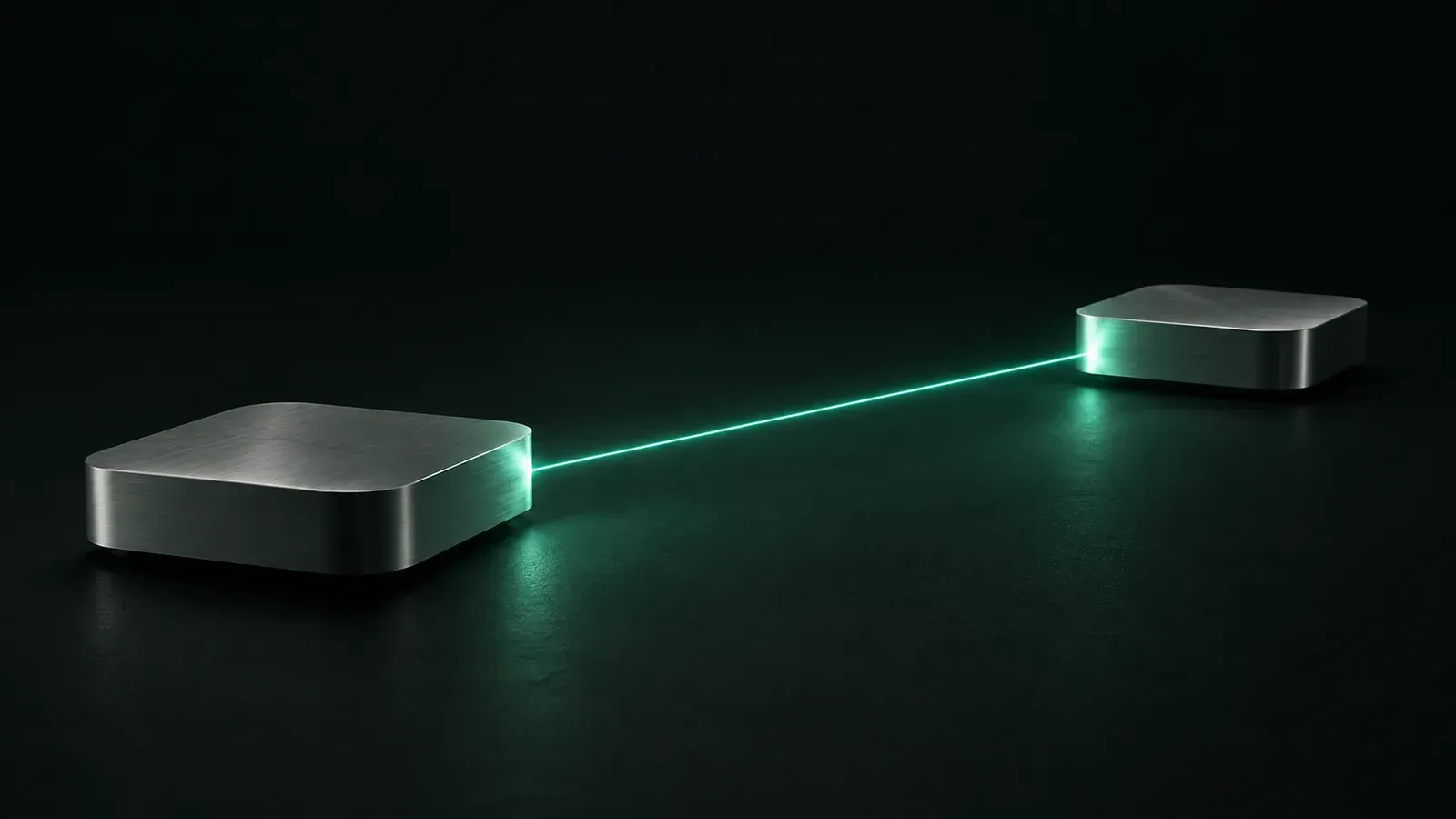 Two rounded aluminium boxes rest on a dark green surface, connected by a thin straight beam of teal light.