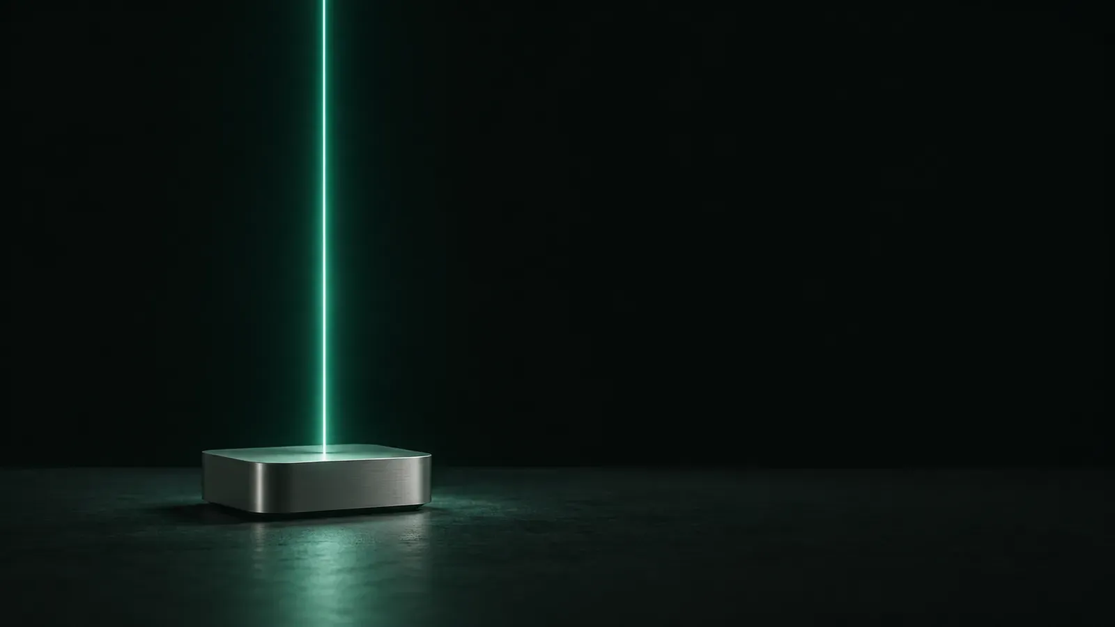 A small rounded silver aluminium box rests on a dark surface as a thin teal beam rises vertically from its top into the darkness.